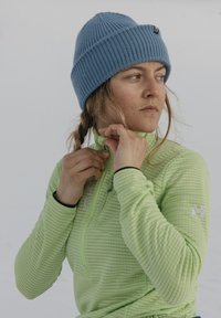 Veste zippée rayée vert clair avec un col montant ; bonnet bleu côtelé ; tissu texturé. Mise au point sur les mains ajustant le zip.