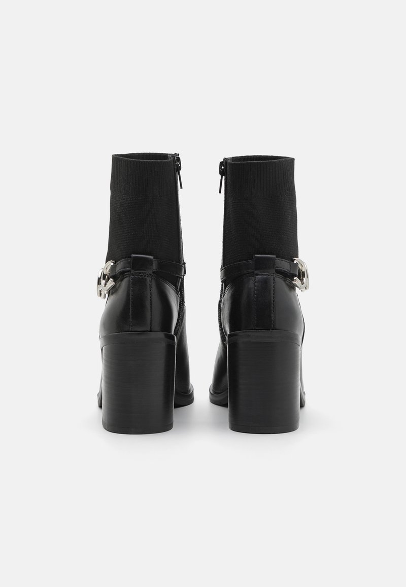 Stivaletti neri con finitura in pelle lucida, parte superiore in maglia elasticizzata e un dettaglio con fibbia argentata di lato. Tacco a blocco e chiusura con zip.