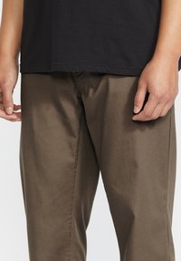 Bruine katoenen broek met een gladde textuur, met een recht model en subtiele stikdetails, gecombineerd met een zwart T-shirt.