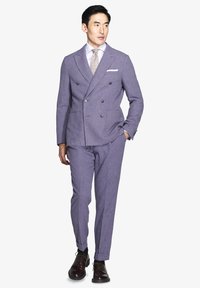 Traje doble pecho de color púrpura claro y textura, con solapas de muesca y bolsillos, combinado con una camisa blanca y una corbata con estampado, finalizado con zapatos oscuros.