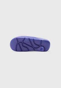 Lilla sneakersåle med et strukturelt gummimateriale og et mønstret slidbane for grep, samt en sirkulær detalj nær hælen.