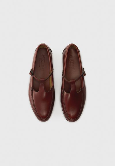 Chaussures en cuir bourgogne avec un bout rond, une sangle élastique et des coutures décoratives le long de la semelle. Texture lisse avec une finition polie.