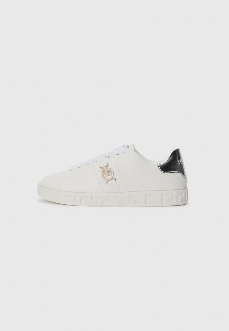 White leather sneaker featuring a rounded toe, gold logo accent, and a black heel cap. Decorative pattern along the white sole.