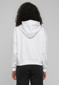 Weißer Kapuzenpullover mit überschnittenen Schultern, gerippten Bündchen und Saum. Glatte Textur; keine sichtbaren Muster oder Marken.