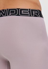 Hellblau-lilafarbene Sportshorts mit einem schwarzen Bund und fetter weißer Schrift. Der Stoff wirkt glatt und eng anliegend.
