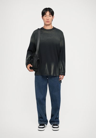 Svart langermet skjorte med en subtil glans, kombinert med løse blå jeans og svart-hvite joggesko. Personen holder en svart veske.