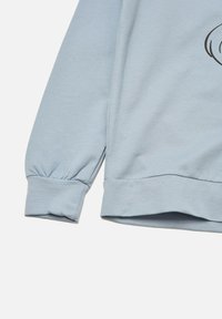 Sudadera de manga larga azul claro con puños elásticos y dobladillo acanalado, mostrando parcialmente un diseño de líneas negras sobre la tela.