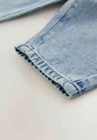 Vaaleansininen farkkuhousujen lahje, jossa on käännetty cuff. Ominaisuuksia näkyvissä olevat saumat ja hieman haalistunut pinta. Puhtaat reunat, ei koristeluja.