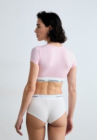 Růžový crop top s krátkým rukávem spárovaný s bílými kalhotkami s vysokým pasem, které mají kontrastní černobílý logo elastický pásek na každém výrobku.