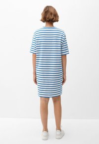 Gestreepte T-shirt jurk met korte mouwen, met blauwe strepen op een witte achtergrond, gemaakt van zachte katoen. Draagt witte sneakers.