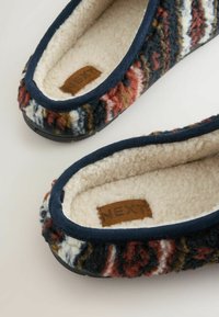 Chlupaté textilní pantofle s vícebarevným vzorem v červené, námořnické, bílé a hnědé barvě. Měkká fleecová podšívka a texturované gumové podrážky.