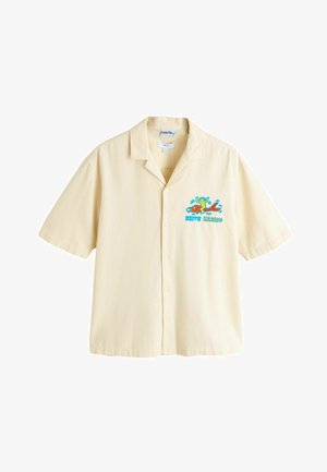 Kremfarvet kortærmet skjorte med knapper og et farverigt Keith Haring-grafik af en figur, der rider på en rød hund, på venstre bryst.