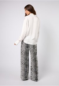 Hvit bluse med lange ermer og volangkrage, kombinert med vide bukser med svart-hvitt leopardmønster.