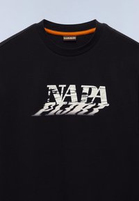 Μαύρο μπλουζάκι με ανάγλυφο, παραμορφωμένο γραφικό τύπωμα της λέξης "NADA" σε λευκό, με πορτοκαλί λεπτομέρειες στον γιακά.