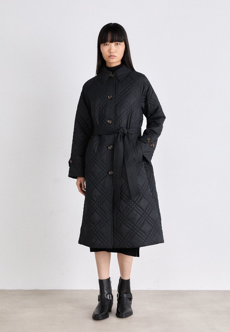 Cappotto lungo nero trapuntato con chiusura a bottoni, vita con cintura e motivo a diamante. Presenta un colletto e maniche lunghe. Design lungo fino alla caviglia.