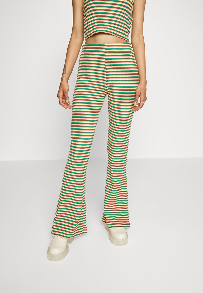 Top cropped riscado e calças largas em malha canelada nas cores verde, vermelho e bege. Apresenta uma cintura ajustada e aberturas largas nas pernas. Sapatos de plataforma em cor creme.