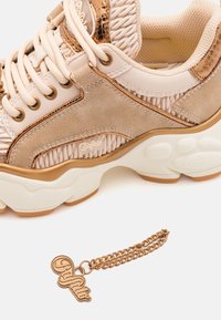 Chunky sneakers in beige and light pink with a textured upper, gold accents, and thick white rubber sole; includes a gold charm keychain.