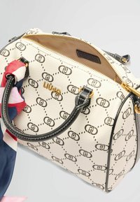 Weißer, strukturierten Handtasche mit schwarzen und goldenen Akzenten. Merkmale ein sich wiederholendes Logo-Muster und ein farbenfrohes Tuch, das an einem Griff gebunden ist.