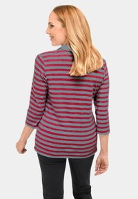 Gestreepte lange mouw top met grijze en rode horizontale strepen, zachte stof en een ronde hals. Draagt met zwarte broek.