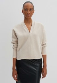 Maglione lavorato a maglia beige con scollatura a V, spalle scese e maniche lunghe, abbinato a una gonna a tubino in pelle nera elegante.