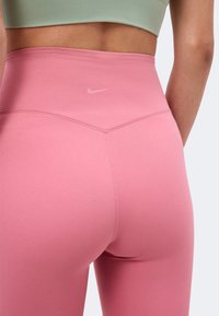 Κοντινό πλάνο ενός ατόμου που φοράει ροζ κολάν Nike με ψηλή μέση και ανοιχτοπράσινο αθλητικό τοπ, εμφανιζόμενο από πίσω.