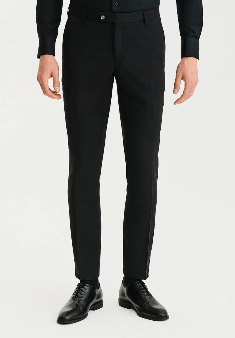 Czarne dopasowane spodnie o prostym kroju, wykonane z gładkiego materiału, z zapięciem na guzik i subtelnymi fałdami z przodu. W połączeniu z czarnymi eleganckimi butami.