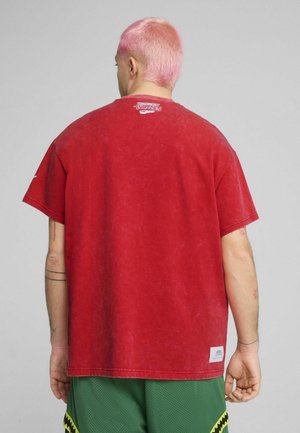 Tricou din bumbac roșu cu croi lejer și umeri căzuți. Prezintă o textură estompată și un logo grafic pe partea superioară a spatelui.