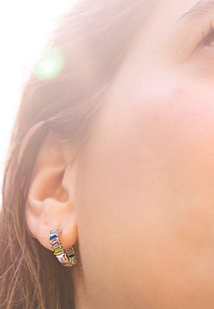 Boucles d'oreilles Huggie avec plusieurs pierres rectangulaires colorées serties dans un métal doré. Le design est courbé, créant un aspect en couches.