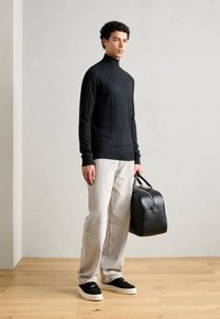 Schwarzer gerippter Rollkragenpullover, hellgraue Jeans und schwarze Sneaker. Hält eine strukturierte schwarze Ledertasche mit Obergriffen und silberner Hardware.