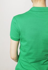 Polo vert en tissu texturé, avec col et manches courtes, présenté de dos. Aucun motif ni accent visible.