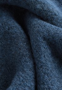 Gros plan d'un tissu en laine bleu foncé doux et texturé avec des fibres visibles et des plis délicats créant des ombres et de la profondeur.