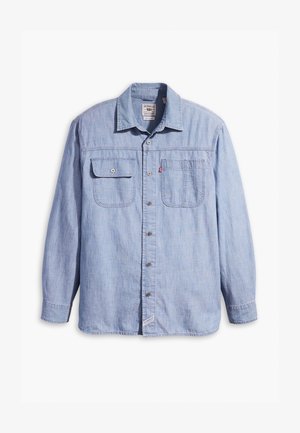 Világoskék farmering, hosszú ujjal, elöl két zsebével fedéllel és egyenes aljjal. Kidolgozott részletek és fémből készült gombok jellemzik.