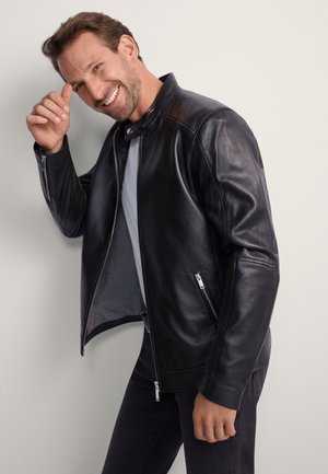 Czarna skórzana kurtka motocyklowa z kieszeniami na zamek i stójką, zestawiona z szarą koszulką i ciemnymi dżinsami.