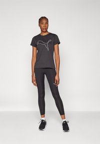 Fekete sport póló fehér Puma logóval, fekete leggings-szel párosítva. Model fekete sportcipőt visel. Sima szövet, egyszerű dizájn.