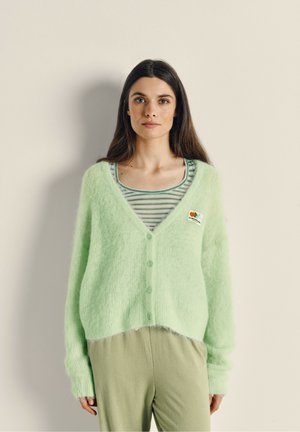 Cardigan vert clair et moelleux à boutons sur le devant, avec un léger col en V et une texture côtelée. Associe à un haut à rayures avec col rond.