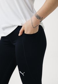 Leggings noirs au design ajusté, dotés d'une poche latérale et du logo Puma en blanc. Le matériau semble lisse et extensible.