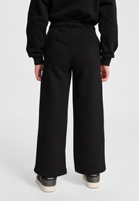 Schwarze Sweatpants mit weitem Bein und elastischem Bund, aus weichem Stoff gefertigt. Sie bieten eine lockere Passform und eine glatte Textur. Kombiniert mit lässigen Turnschuhen.