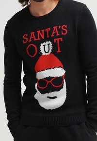 Schwarzer Strickpullover mit rotem und weißem "SANTA'S OUT"-Text und einem Santa-Gesicht mit Sonnenbrille und rotem Hut.