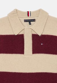 Polo tricotat cu dungi crem și burgundy, cu guler cu nervuri, prezentând un detaliu mic cu logo pe piept și un material texturat.