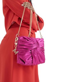 Bolso de satén magenta con un diseño fruncido, correa de cadena dorada y acentos de hardware metálico, que presenta un charm decorativo con "M."