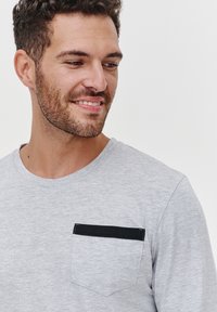 Szary longsleeve w miękkim materiale z czarną kieszonką z białym przeszyciem. Okrągły dekolt i luźny krój.