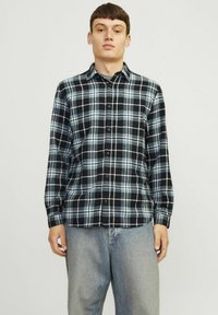 Camisa de franela a cuadros en negro y azul con diseño de botón, mangas largas y cuello. La tela parece suave y tiene un patrón a cuadros.