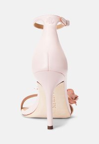Jasnoróżowe sandały na wysokim obcasie z paskiem na kostkę. Gładka skóra, otwarty tył i dekoracyjny detal w postaci falbanki. Błyszczące wykończenie obcasa.