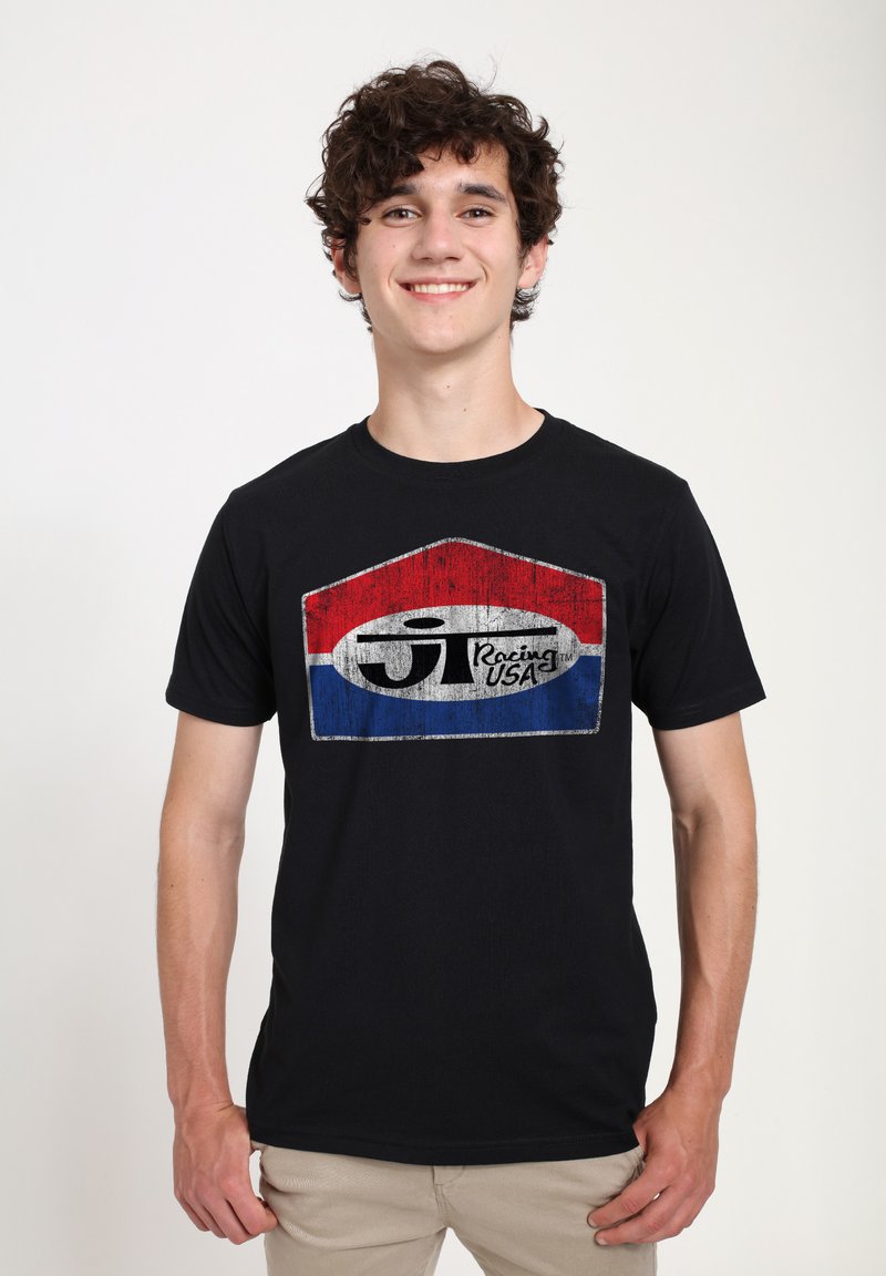 Černé tričko s poškozenou grafikou v červené, bílé a modré barvě, na kterém je v tučném stylizovaném písmu nápis "ST Racing USA".