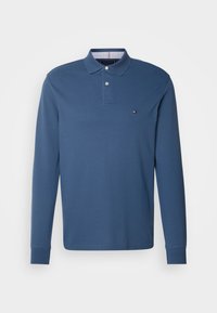 Koszulka polo z długim rękawem w kolorze granatowym, wykonana z bawełny. Posiada zapięcie na guziki oraz małe logo na piersi. Gładka tekstura.