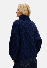 Granatowy sweter z wysokim kołnierzem i wzorem warkocza. Gruba tekstura z szerokimi rękawami i dopasowanym dołem.