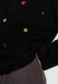 Pull noir avec broderie colorée, comportant des points roses, bleus, verts, jaunes et violets. Texture douce avec une coupe décontractée et un ourlet côtelé.
