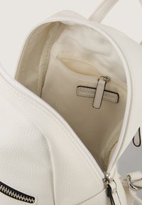 Witte textuur van de binnenkant van de rugzak met een ritsvak, gladde voering en een label. De buitenkant heeft een contrasterende zwarte ritsdetail.