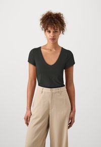T-shirt noir à manches courtes et col en V en tissu doux, associé à un pantalon large taille haute beige avec une fermeture à un bouton.