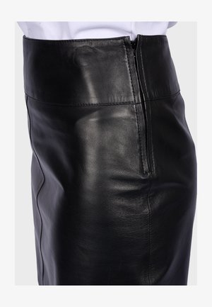 Zwarte leren rok met hoge taille en zijrits, gedragen met een wit ingestopt overhemd op een neutrale achtergrond.